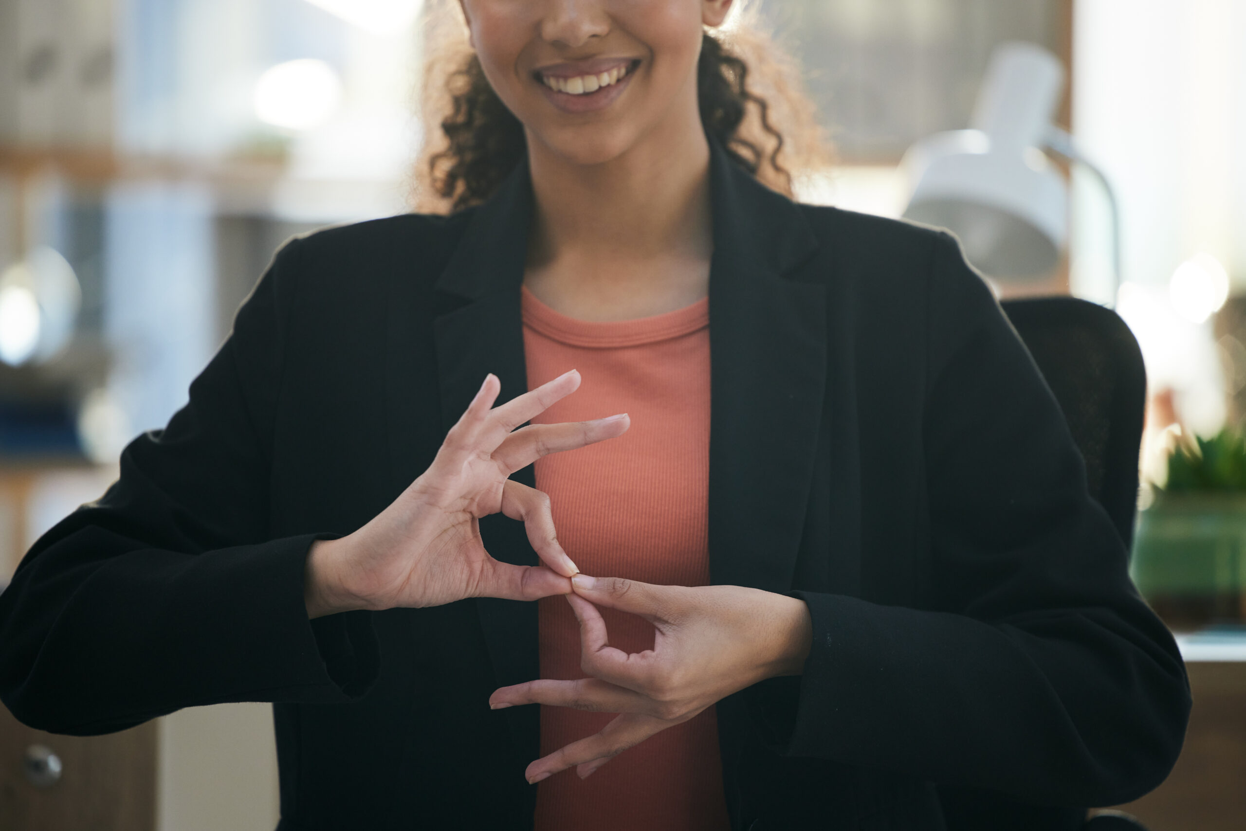 A woman in a professional setting demonstrating ASL with hand gestures, representing the importance of ASL interpreting services for effective communication.